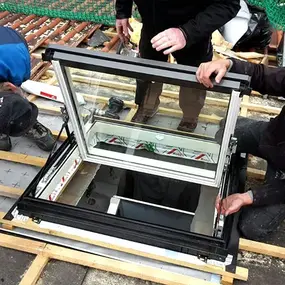Drei Handwerker montieren ein modernes Dachfenster in ein Ziegeldach auf einer Baustelle.