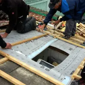 Handwerker montieren Dachfenster und Dämmung bei einer energetischen Dachsanierung.