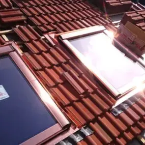Zwei neue Dachfenster werden in ein Ziegeldach eingebaut, Sonnenlicht reflektiert.