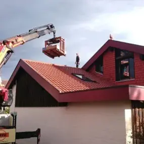 Ein Baukran hebt Baumaterial auf das Dach eines Einfamilienhauses zur Dachsanierung.