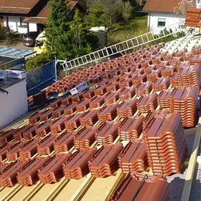 Dachdeckerarbeiten mit gestapelten Dachziegeln auf einem Neubau-Dach in Wohnsiedlung.