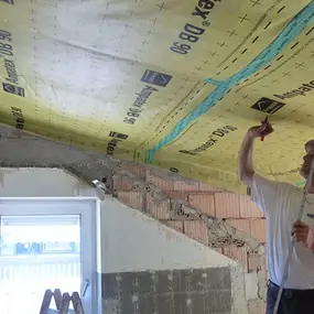 Ein Handwerker bringt Dampfbremse im Dachgeschoss zur energetischen Dämmung an.