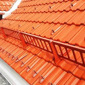 Rotes Ziegeldach mit Schneefangsystem und Dachrinnen, ideal für Dachschutz und Sicherheit.