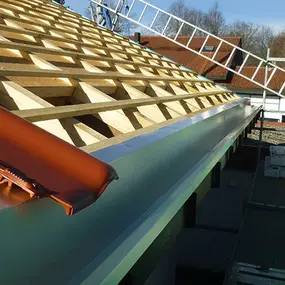 Dachkonstruktion mit Holzlattung, Regenrinne und Ziegel auf einer Baustelle im Rohbau.