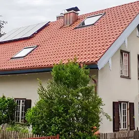 Einfamilienhaus mit rotem Ziegeldach, Solaranlage und Fenstern, umgeben von Garten.