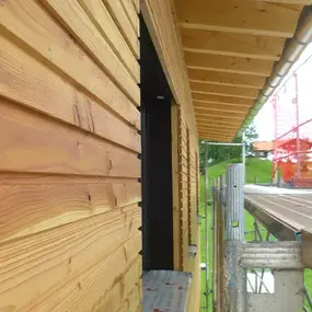 Fassade aus Holz mit waagerechter Verschalung an einem Gebäude neben Baugerüst und Dach.