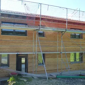 Modernes Holzhaus mit Baugerüst auf einer Baustelle in ländlicher Umgebung im Sommer.