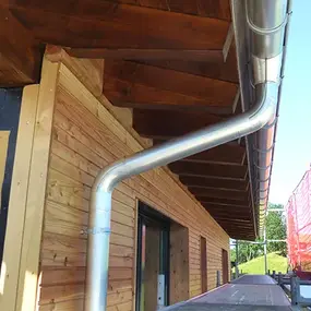 Holzhaus mit moderner Dachrinne, Fassadendämmung und Baugerüst auf Baustelle.