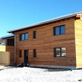 Modernes Holzhaus mit Flachdach und Garage im Winter auf verschneitem Grundstück.