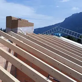 Holzdachstuhl auf Rohbau mit Blick auf Berge und blauen Himmel beim Hausbau.
