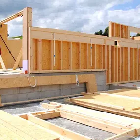 Holzrahmenbau eines Einfamilienhauses auf Bodenplatte bei sonnigem Wetter und grüner Landschaft.